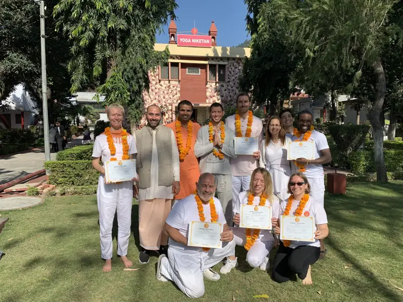 Teacher training graduates with certificates and marigold garlands in the ashram garden