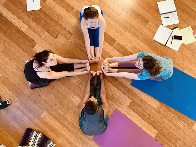 Four students in a forward fold with feet meeting in a circle, seen from above