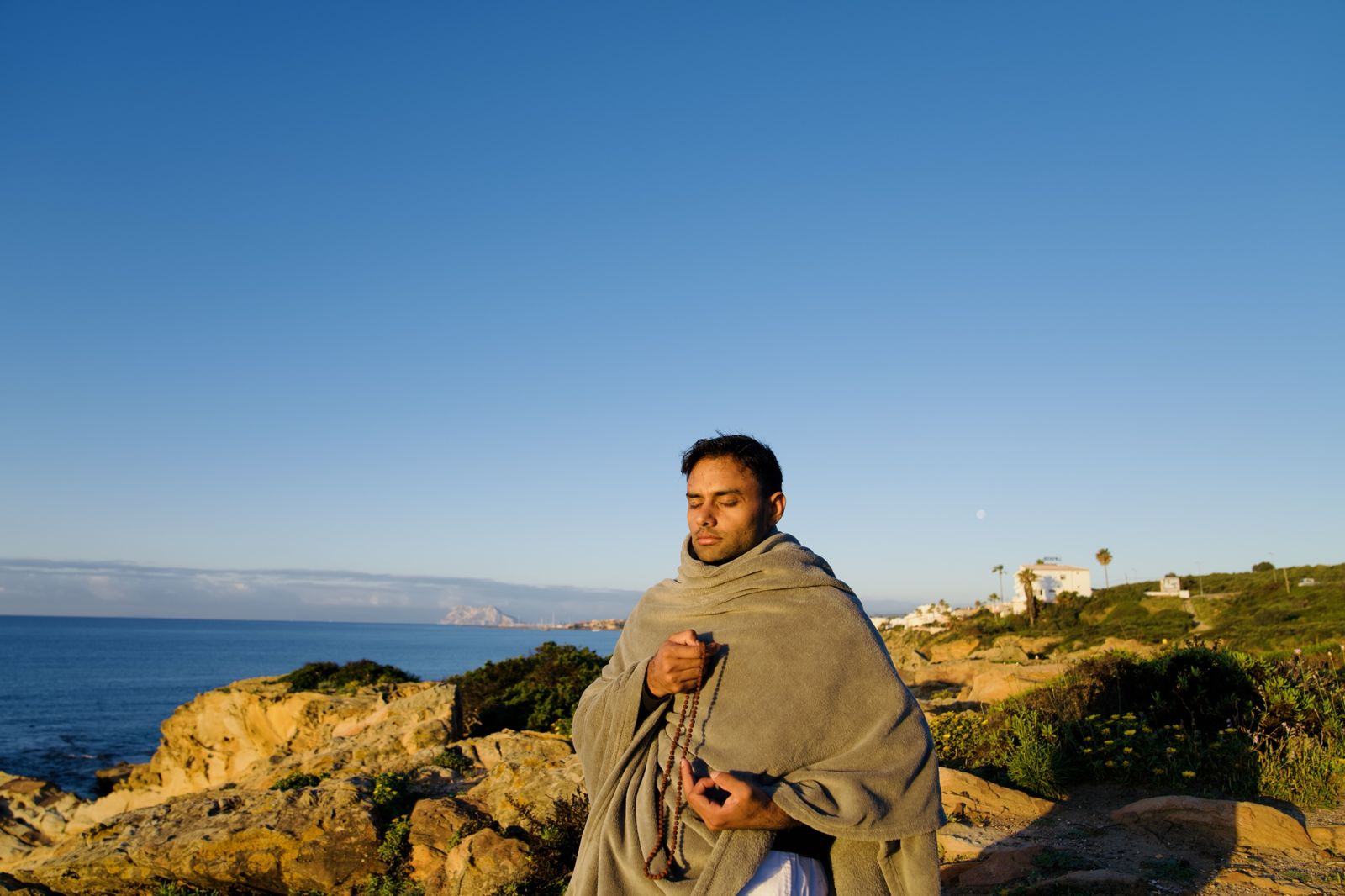 A teacher meditating with a mala on the coast at sunrise