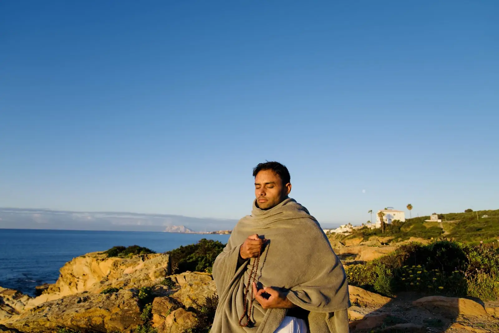 A teacher meditating with a mala on the coast at sunrise
