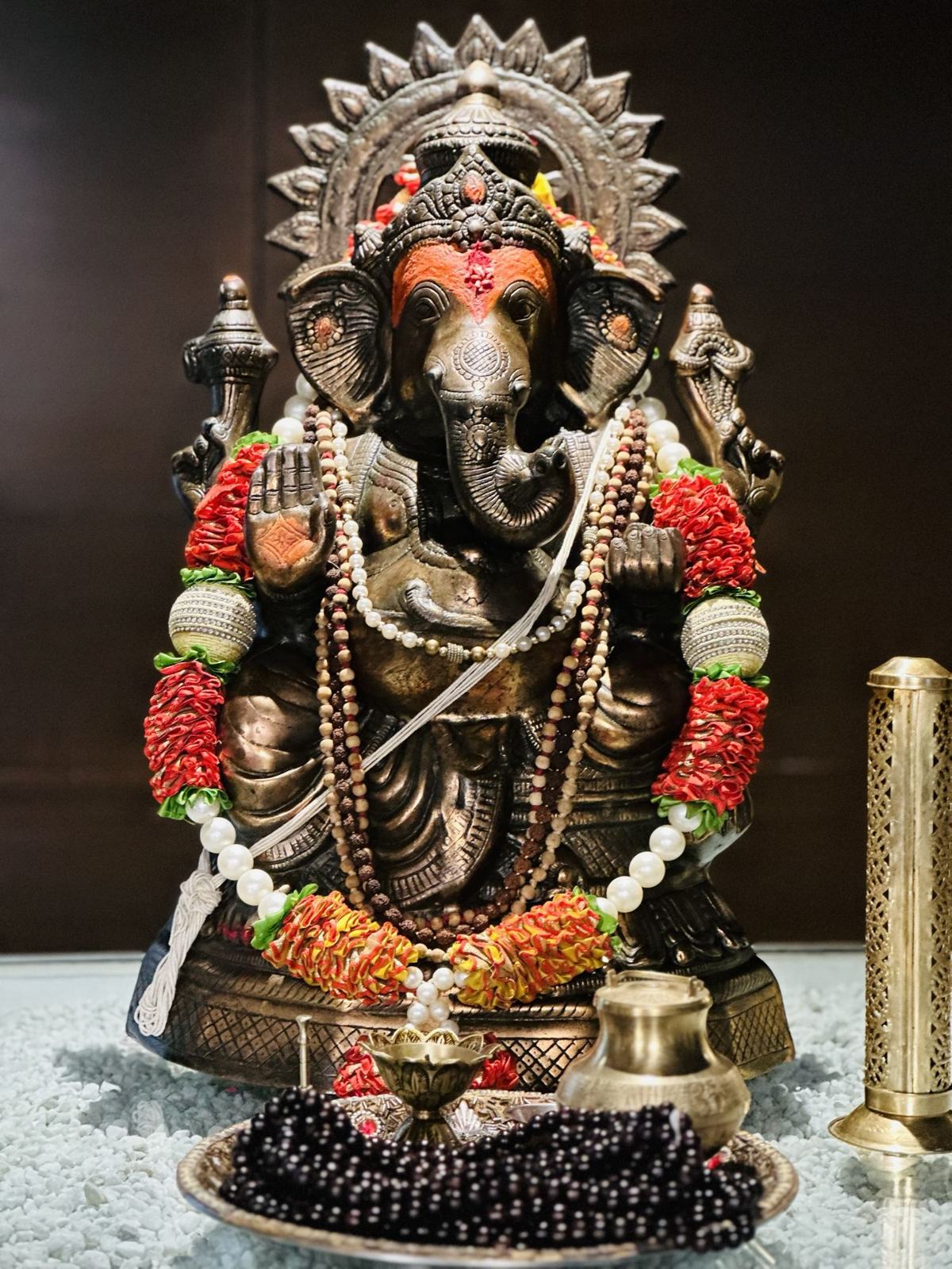 A brass Ganesha adorned with garlands and malas