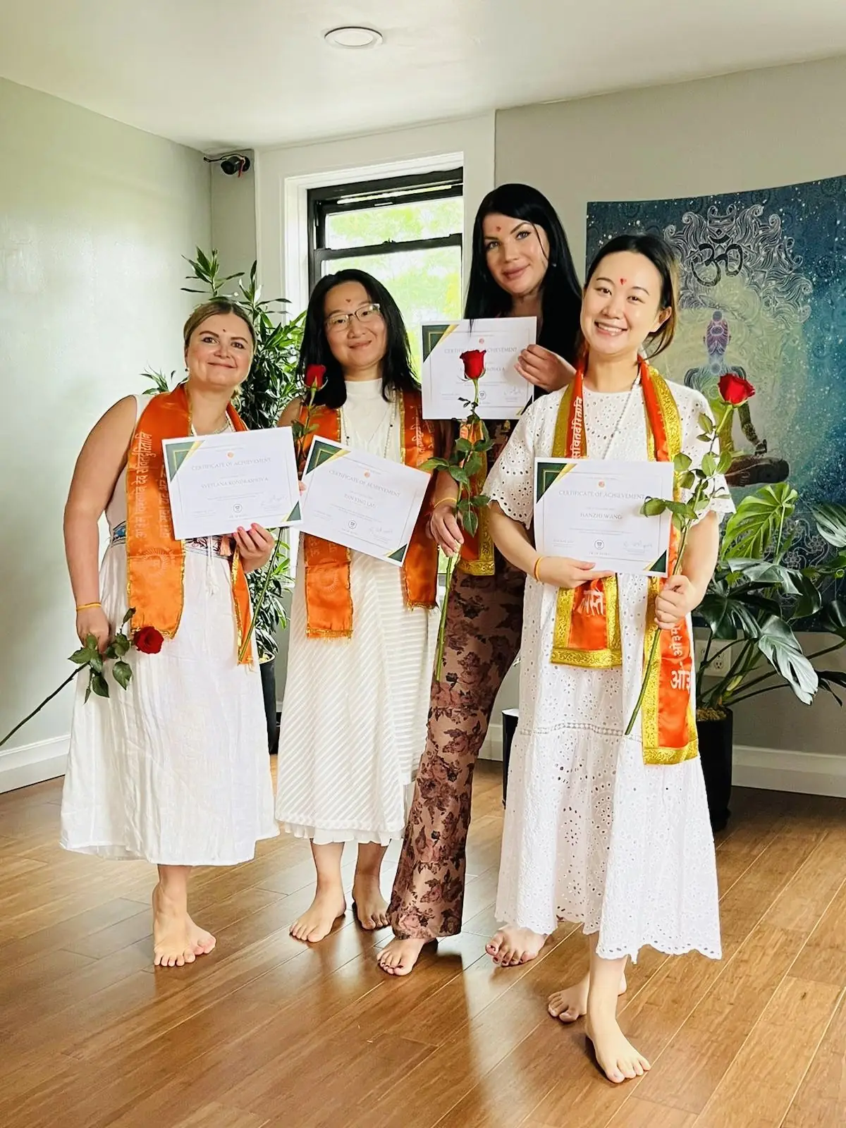 Four graduates in orange stoles holding certificates and roses