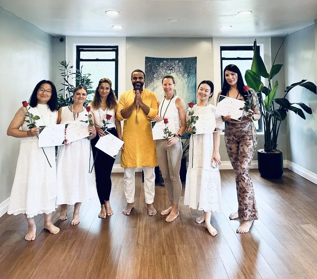 A teacher in a yellow kurta with namaste hands among graduates holding certificates and roses