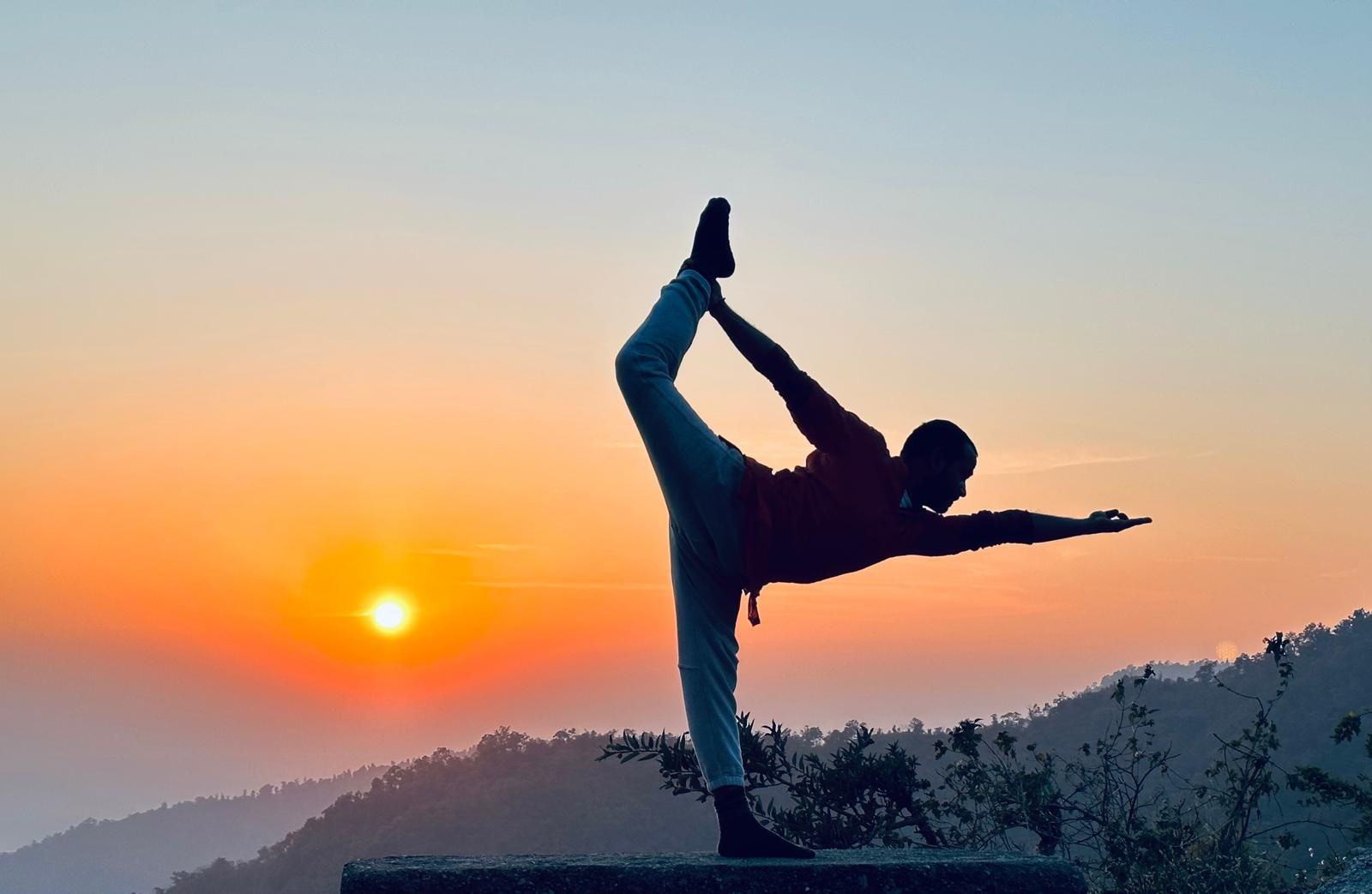 A yogi in dancer pose silhouetted against the sunrise over the Himalayan foothills