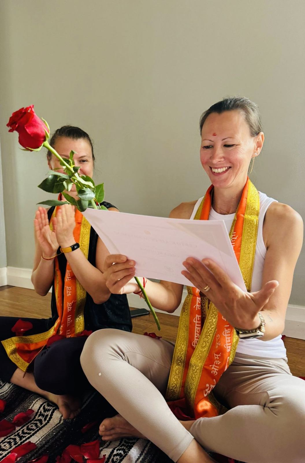 A graduate beaming at her certificate as a friend applauds with a rose