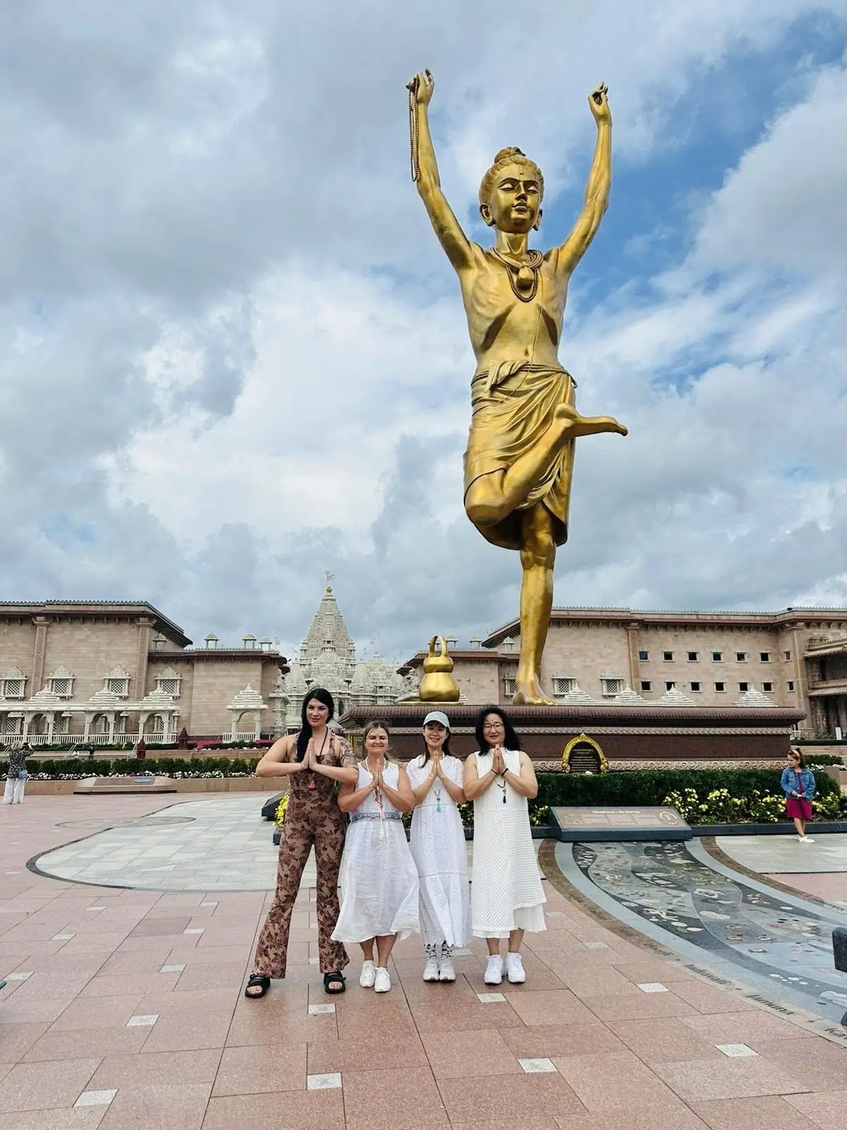 Graduates in namaste before a golden statue at the temple
