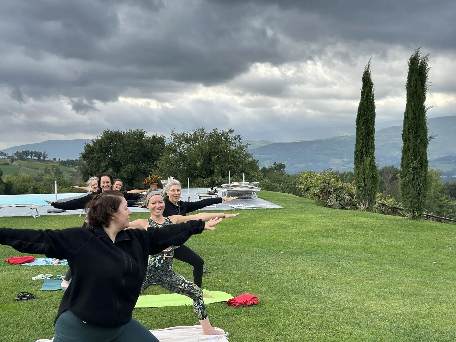 The group in warrior II on the lawn, cypress trees and hills behind
