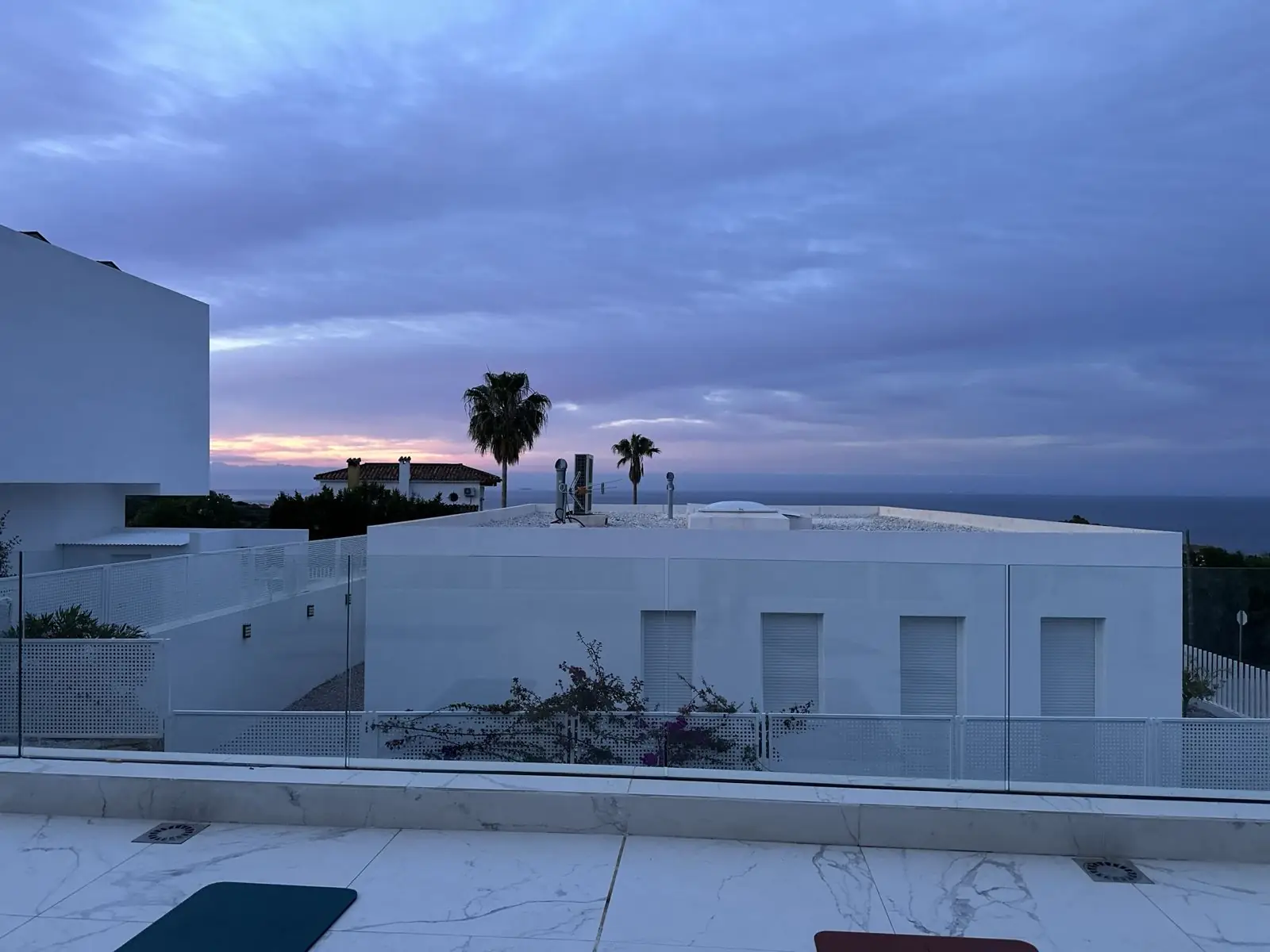 Yoga mats on the marble terrace at dawn, looking over palms to the sea